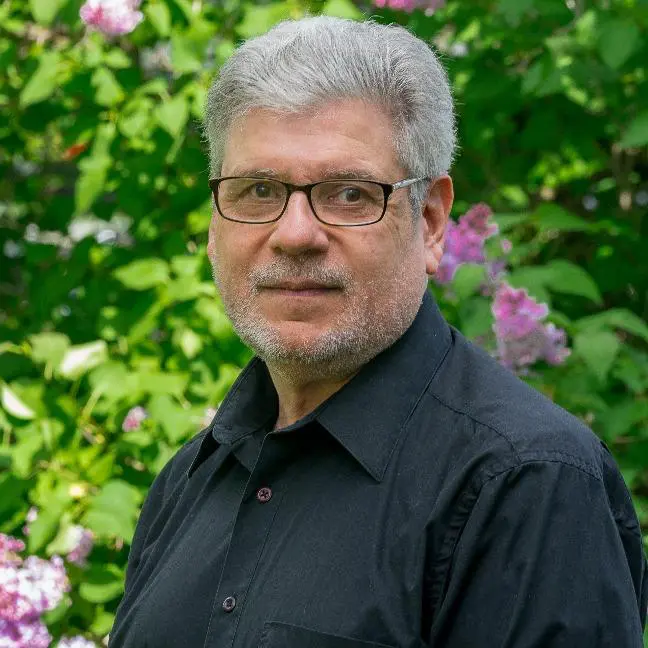 A man with glasses standing in front of some bushes